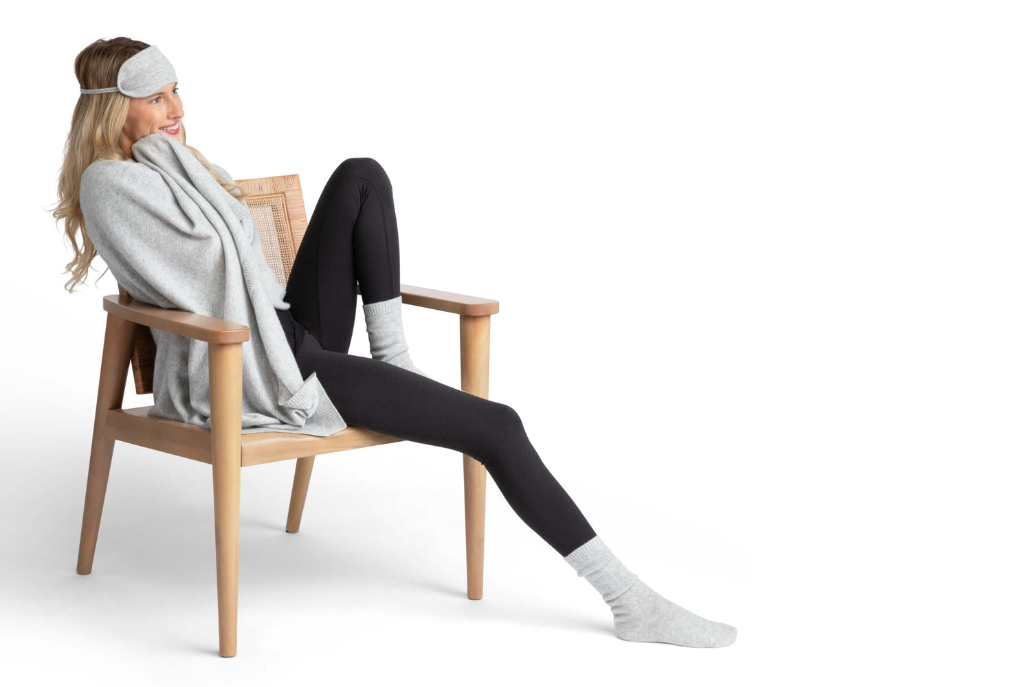 Woman sitting on a chair wearing a gray cashmere eye mask, blanket, and black leggings with gray socks.